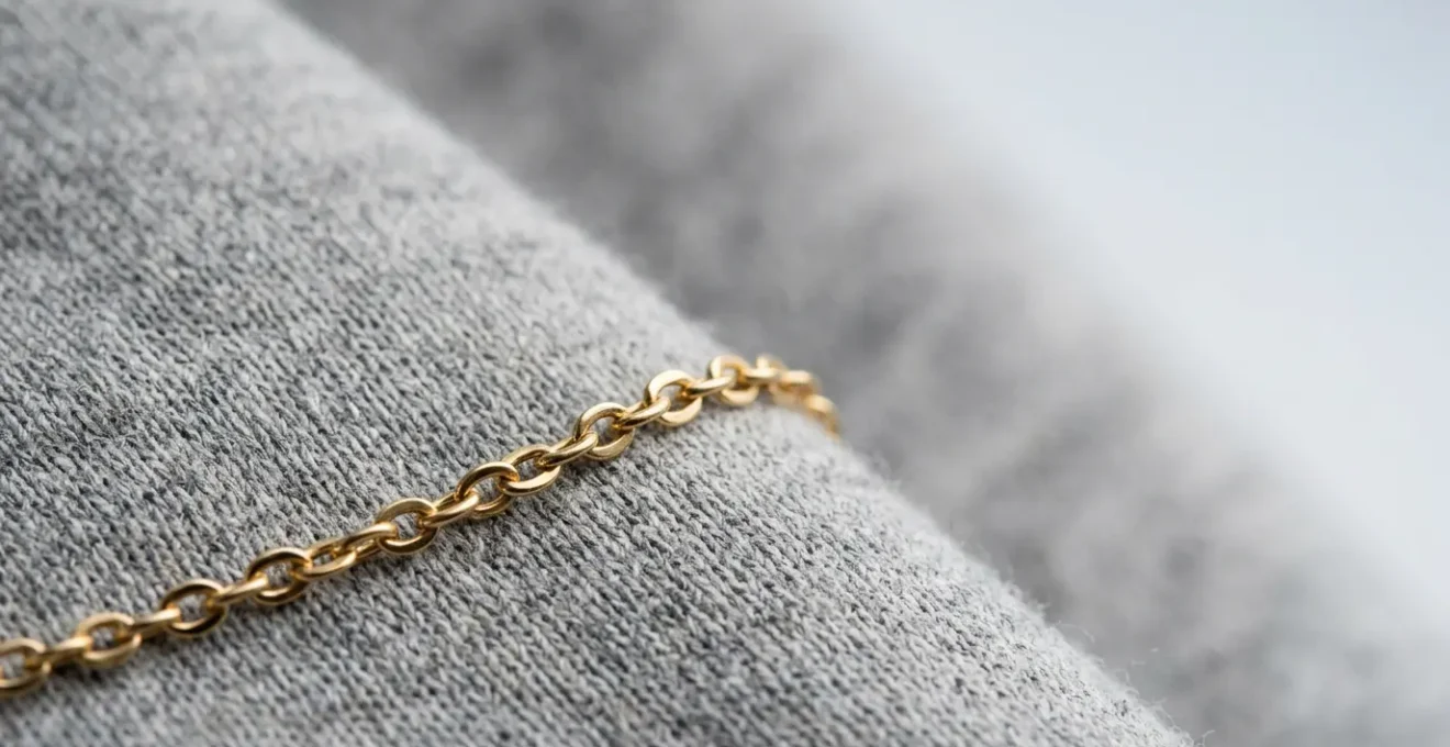 Nahaufnahme einer feinen Goldkette auf hochwertigem grauem Hoodie-Stoff, natürliches Licht