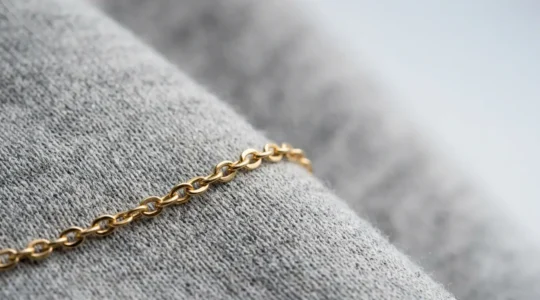 Nahaufnahme einer feinen Goldkette auf hochwertigem grauem Hoodie-Stoff, natürliches Licht