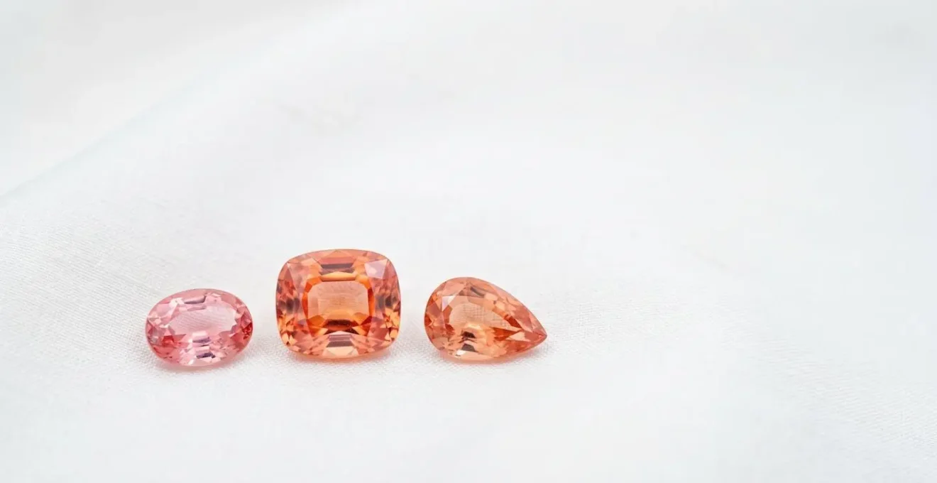 Padparadscha-Saphire in verschiedenen Rosa-Orange-Nuancen nebeneinander auf neutralem Hintergrund
